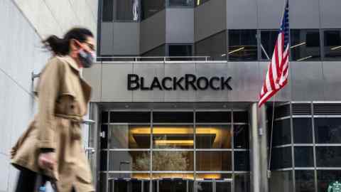 A pedestrian wearing a protective mask passes in front of BlackRock’s headquarters in New York