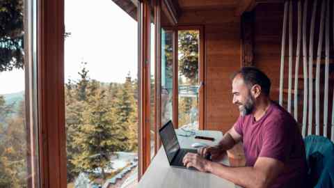 man working on a laptop from his cabin in the woods