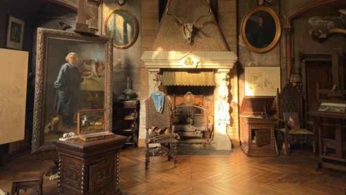 A partially-sunlit room with an ancient fireplace, gold-framed paintings on the walls and old wooden furniture