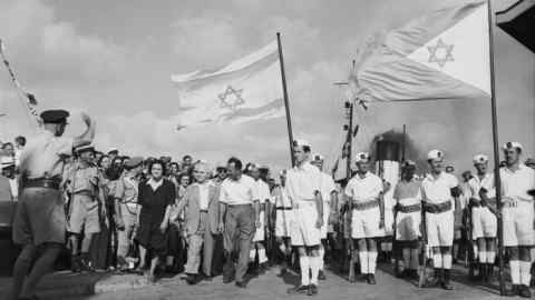 Israeli prime minister David Ben-Gurion walks flanked by a large crowd at the Haifa docks to see the last contingent of British troops depart in 1948