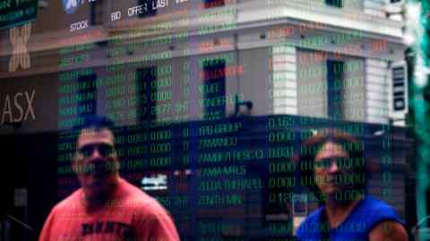 Pedestrians are reflected against an electronic board displaying stock information inside the Australian Securities Exchange