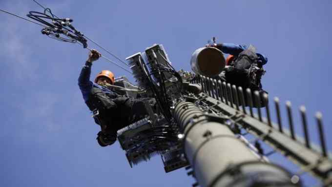 Engineers scale a telecommunication network mast to install 5G apparatus