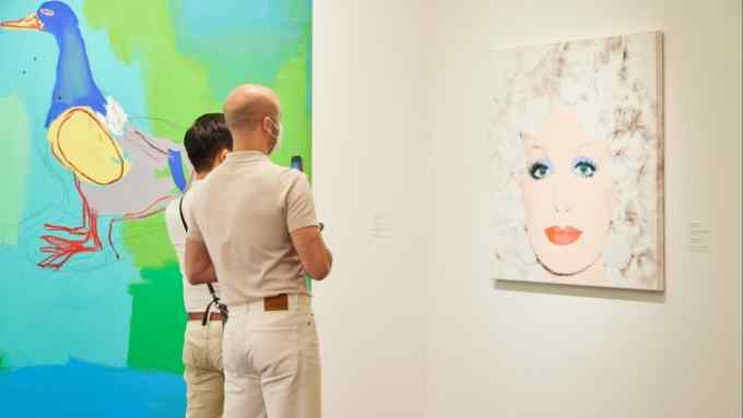 Two people look at a screenprint of a blonde woman with bright red lips