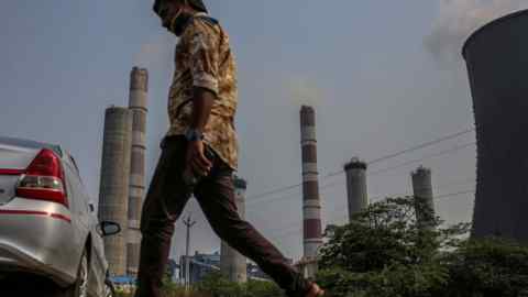 A man walks past chimneys and a cooling tower