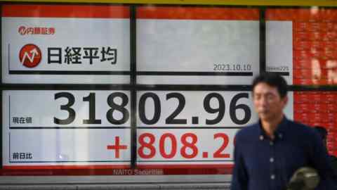A man walks in front of an electronic board showing numbers of the Tokyo Stock Exchange