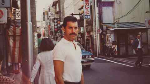 A man with a moustache stands on a street in Tokyo