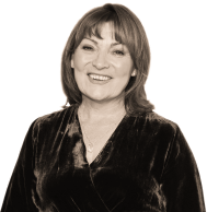 A portrait of Lorraine Kelly CBE, a white woman with long dark hair, wearing a jacket, and smiling at the camera